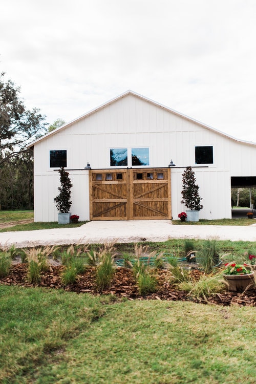 white barn with large wooden doors with beautiful garden out front